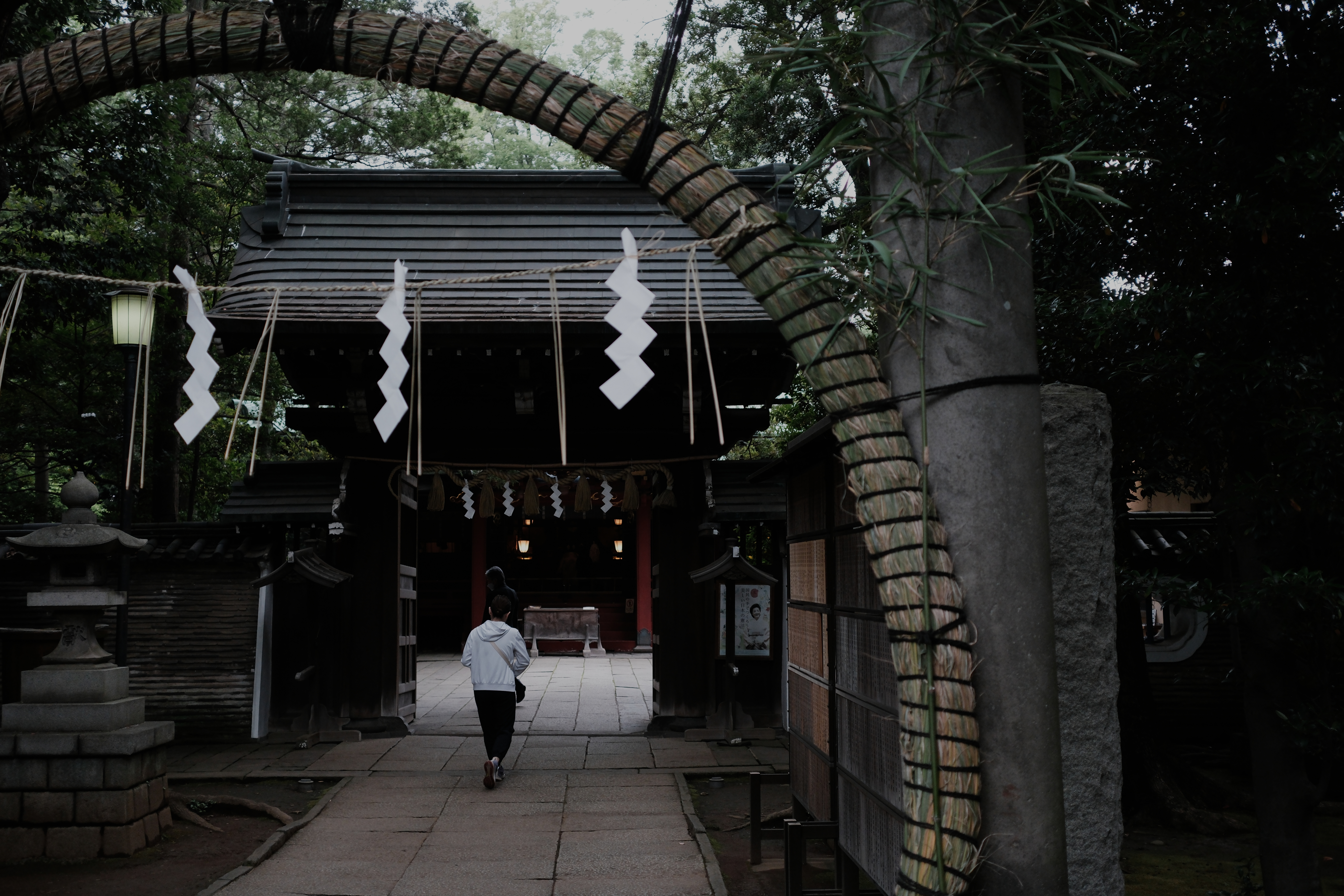 Figure walking through a shimenawa rope arch toward a temple