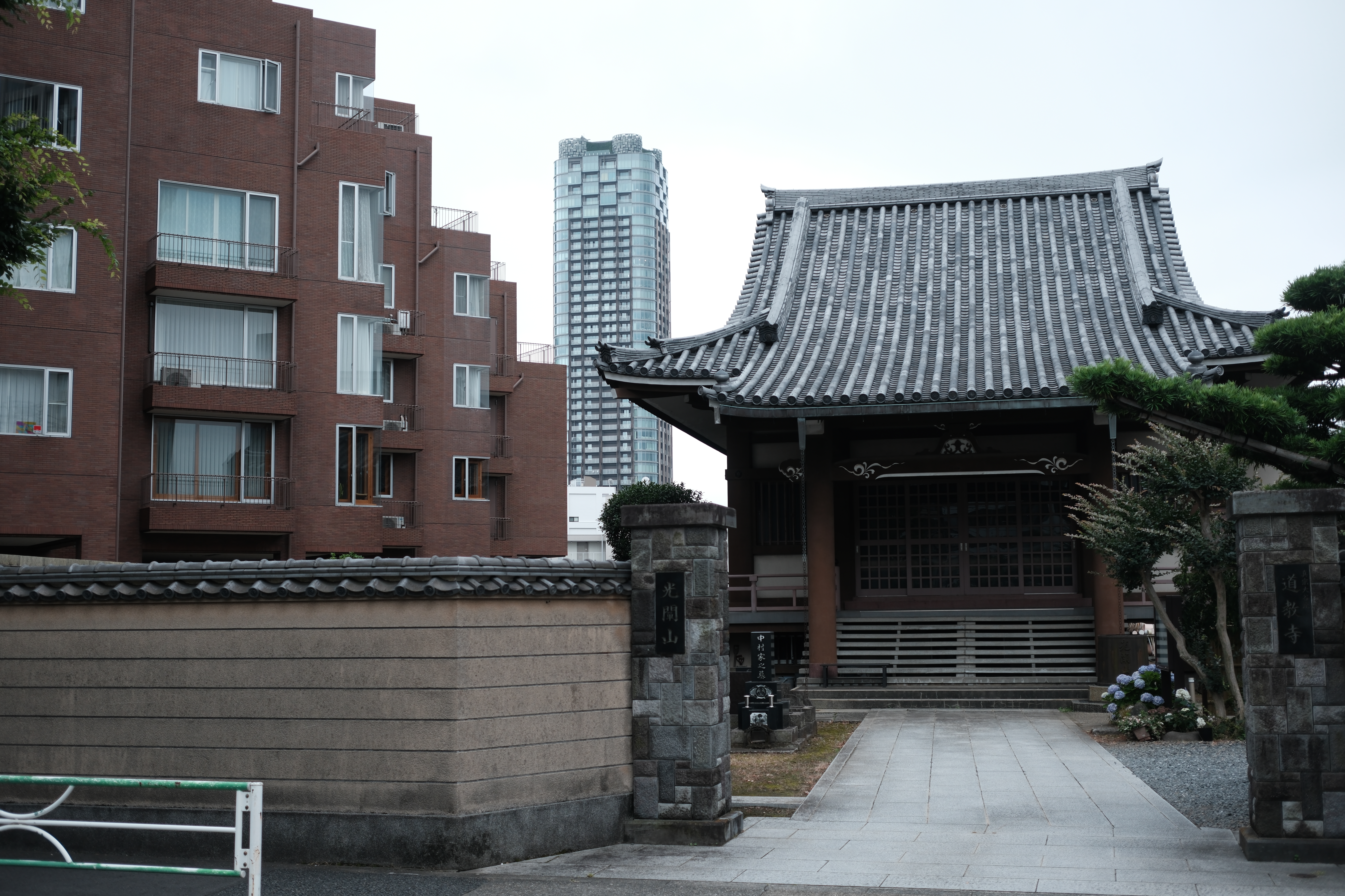 Stone gate and wall at Dokyo-ji, an apartment block and glass tower close behind