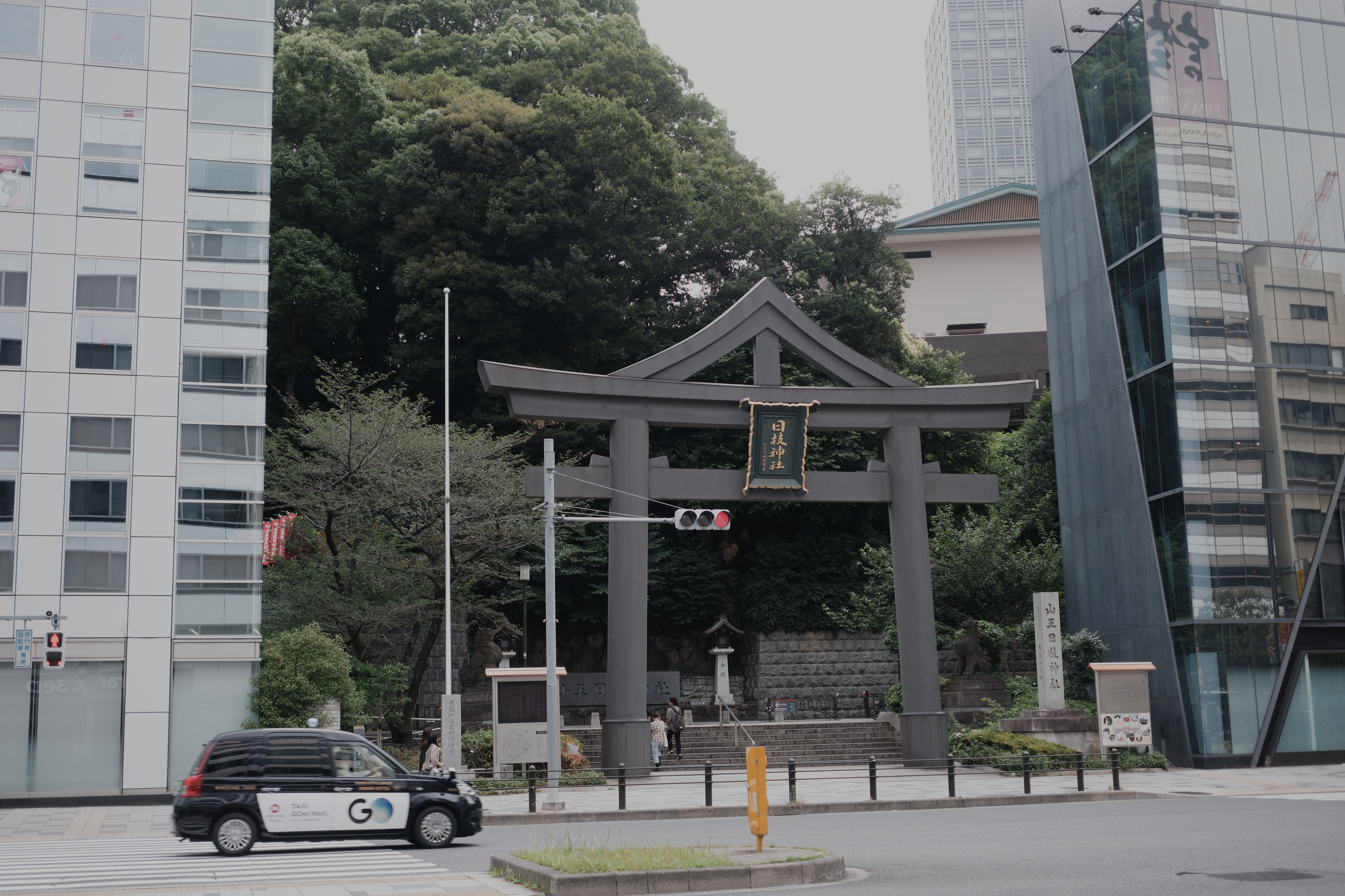 Torii gate at the end of a narrow street, a taxi passing through frame