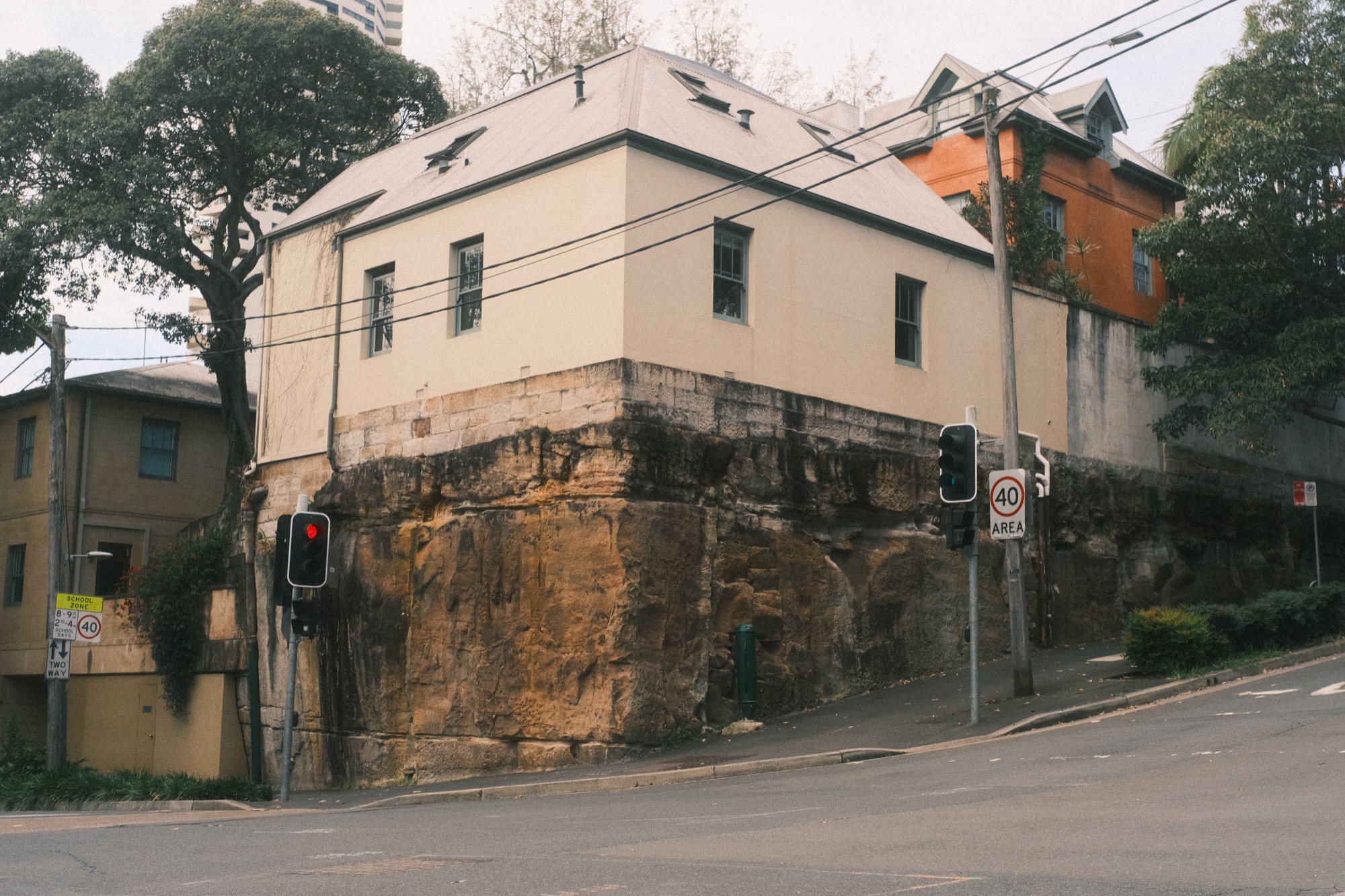 A house stands on a base of bare sandstone above a street corner.